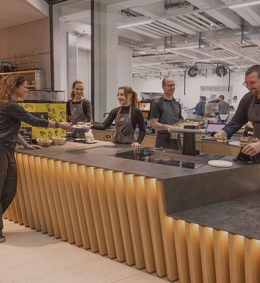 Team des café unique hinter der Theke in Action mit der Produktion im Hintergrund